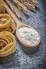 Wheat rye ears wooden spoon flour uncooked twisted macaroni on b