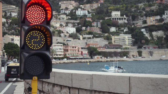 Stop red signal  at a traffic light. Mediterranean city view.  Boat along shore. Area close to the seaside with cars on the road.