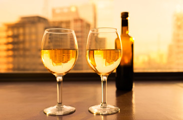 Glasses of white wine and bottle with city view.
