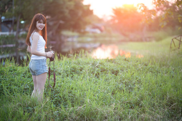 Cute Asian woman with long brown hair holding a camera in the wild in the sunset.