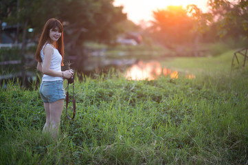 Cute Asian woman with long brown hair holding a camera in the wild in the sunset.