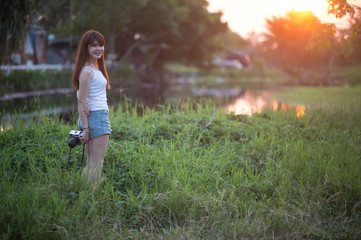 Naklejka na ściany i meble Cute Asian woman with long brown hair holding a camera in the wild in the sunset.
