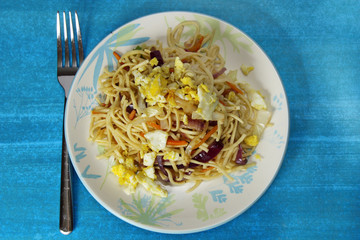 Chinese noodles or chowmien with eggs and vegetables in a bowl on blue  background with copy space.