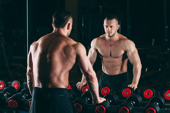 Muscular man out in gym standing near dumbbells , strong male naked torso abs