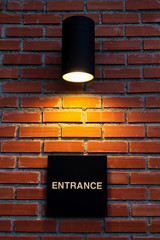Black entrance sign with lamp lighting on brick wall background