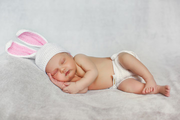 Peaceful sleep of a newborn baby in the grey beds,cute baby in hat with Bunny ears, sleeping sweetly tucked arms and legs on grey background