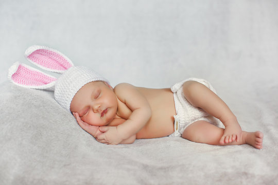 Peaceful sleep of a newborn baby in the grey beds,cute baby in hat with Bunny ears, sleeping sweetly tucked arms and legs on grey background