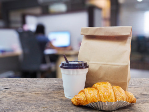 Coffee And Croissant With Paper Bag On Wooden Table