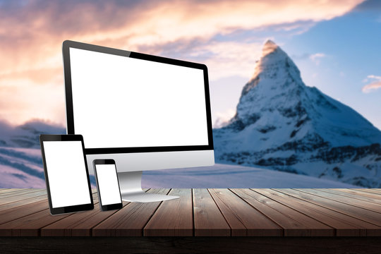 Computer display, tablet and smart phone responsive display devices on table. Isolated white screen for mockup presentation. Mountain nature landscape in background