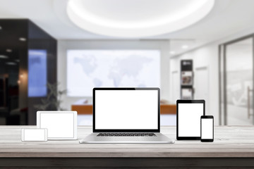Laptop, tablet and smart phone responsive display devices on table. Isolated white screen for mockup presentation. Office interior in background