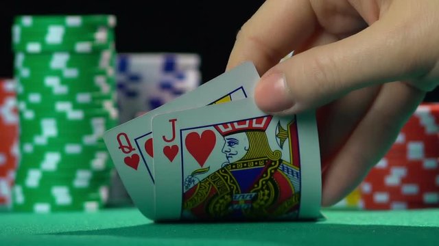 Poker player showing cards, queen and jack of hearts. Unequal love, misalliance