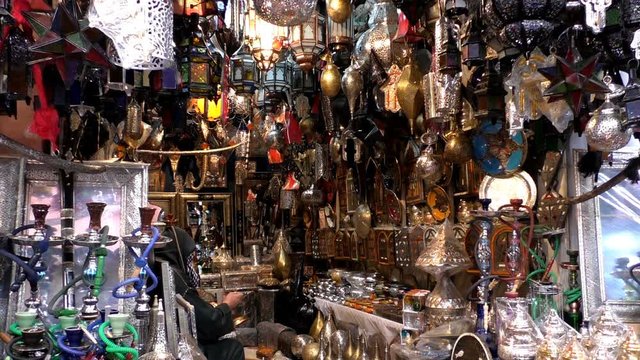 Moroccan Berber man wearing traditional hooded djellaba dress sitting in the lights and lanterns shop at the Marakesh Marakech market and working