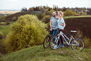 Fototapeta premium Beautiful young couple in love walking with bicycles,standing and hugging near the Bicycle and consider nature. The concept of active rest