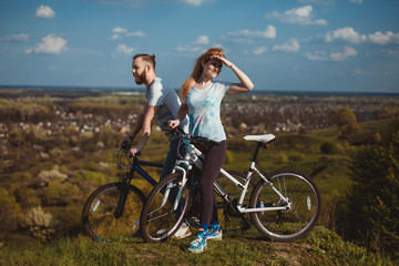 Fototapeta premium Beautiful young couple in love walking with bicycles, looking towards the beautiful nature and the blue sky. The concept of active rest