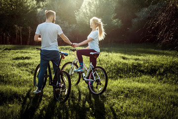 Fototapeta premium Beautiful young couple in love walking with bicycles, holding hands and talking. Stand near the bikes. The concept of active rest