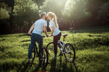 Naklejka premium Beautiful young couple in love walking with bicycles, kissing and hugging. Stand near the bikes. The concept of active rest