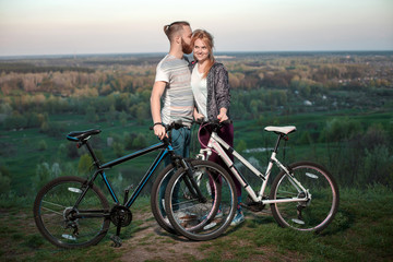 Obraz premium Beautiful young loving couple hugging at sunset, there are two bikes. The concept of happiness, peace and love