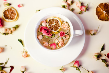 Herbal tea in white Cup and saucer with roses and dried flowers dried round slices of lemon laid on a white background