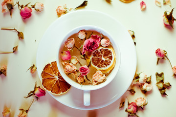 Herbal tea in white Cup and saucer with roses and dried flowers dried round slices of lemon laid on a white background