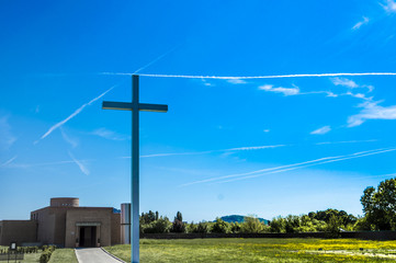 Detail of a religious cross while a cross is designed in the sky by a trail of two airplanes