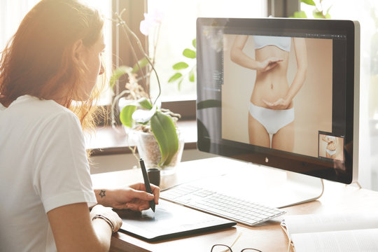 Side View Portrait Of Attractive Woman Retoucher Working On The Computer, Hand Drawing On Graphic Tablet. Young Caucasian Female Photographer With Red Hair In White T-shirt Editing Photos At Home