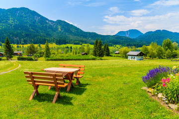 Benches with picnic table on green grass in alpine village on shore of Weissensee lake in summer...