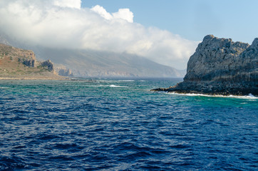 The rocky coast of the Mediterranean sea against the blue sky and clouds.