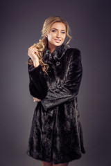 Fashion seductive blond hair lady in an elegant fur coat and bla