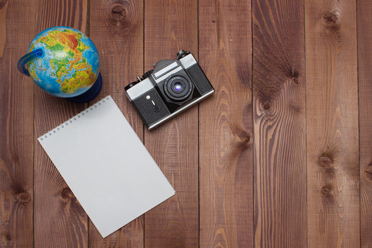 empty notepad, retro camera and globe on brown wooden background