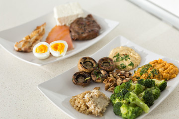 animal versus plant proteins: one plate with beef, eggs, salmon, cheese and chicken grill and another with nuts, mushrooms, broccoli, lentil, hummus and quinoa