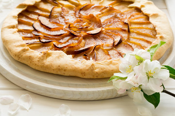 Open pie or galette with apples decorated apple blossom on white wooden desk