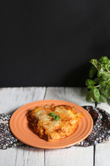 Homemade lasagna, made with Bolognese sauce and Bechamel sauce. Orange plate, white rustic table, decorated with some basil. Selective focus. 