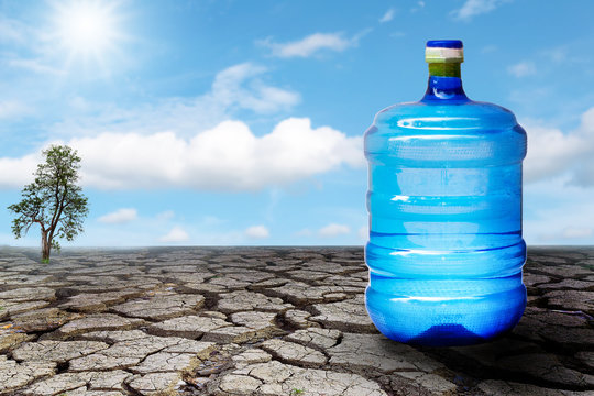 Large plastic water bottle on the ground, dry and cracked with blue sky background.