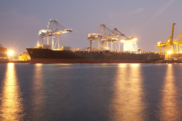 Fototapeta na wymiar Big ship in harbour using cranes loading containers in night time