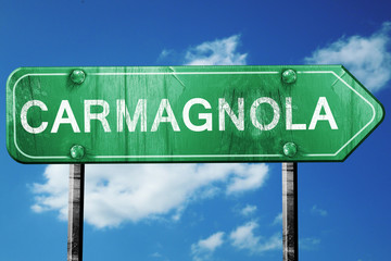 Carmagnola road sign, vintage green with clouds background