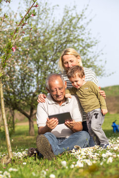Grandparents with grandson enjoying the sunny spring day outdoors. They are looking something on tablet.