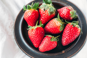 
Whole red ripe strawberries in a black bowl on a white background