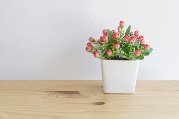 the artificial flower in the white pot on the wooden table with