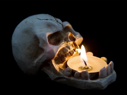 Halloween image with a burning candle on an ancient skull Death concept.  skull near lighting candle on dark background