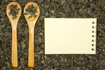 Dry green tea, a blank sheet of paper and a wooden spoon. Place for text