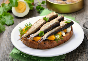 Sandwich with sprats and egg on wooden table