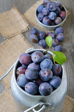 Fresh plums in bowl on the wooden table, top view