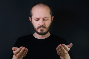 Portrait of an adult man with beard and mustaches on black background, eyes closed, praying and contemplating