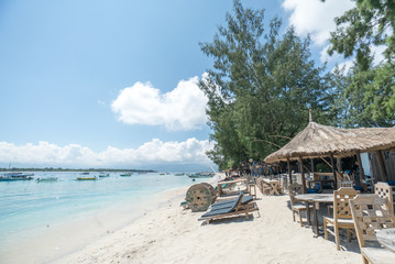 Tropical sandy beach with buildings and boats in a sea. Gili Tra