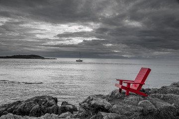 Red chair contrasting with black and white ocean background.