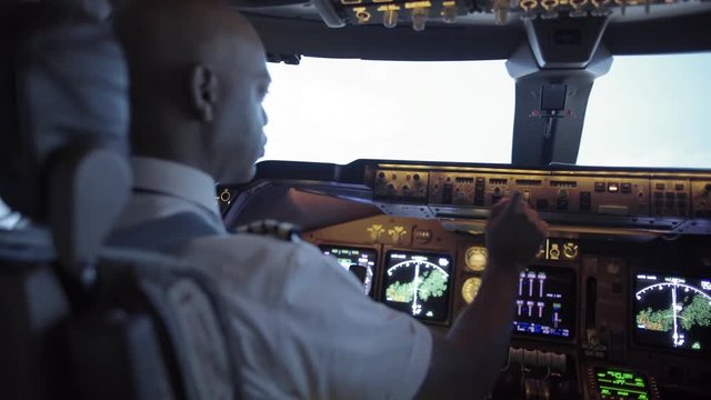 Rear angle view over pilot's shoulder with racking focus from face to instrument panel as he adjusts navigation controls while flying a jumbo jet.  Hand-held camera, recorded in 4K at 24fps.