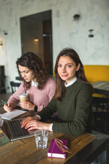 Fototapeta premium Young pretty females working with notes and laptop in cafe