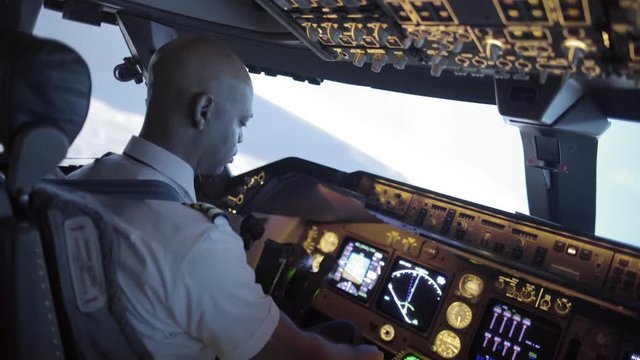 Rear angle view over pilot's shoulder as he adjusts instruments and flies a jumbo jet.  Hand-held camera with racking focus, originally recorded in 4K at 24fps.