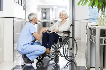 Physiotherapist Holding Smiling Senior Woman's Hand On Wheelchai