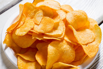 Potato chips on a plate. White plate with yellow chips. Fast snack at new diner. Good example of processed food.